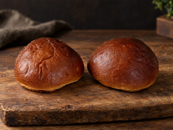 Twee Potato Buns met een glanzende bruine korst op een rustieke houten plank.