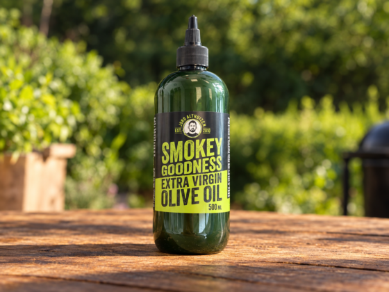 Groene knijpfles Smokey Goodness Extra Virgin Olive Oil op een houten tafel in een zonnige tuin