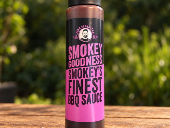 Fles Smokey Goodness Smokey's Finest BBQ Sauce op een houten tafel in een groene buitenomgeving